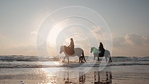 SLOW MOTION. silhouette of women riding beautiful horses wading through the sea splashing water drops around in golden