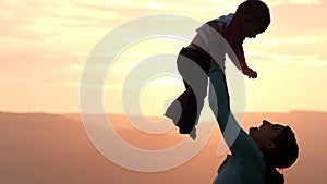 Slow motion of silhouette of a young woman rocking her baby at sunset.