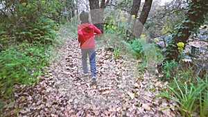 Slow motion of six year old boy seen from behind running in the woods wearing a red sports suit