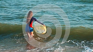 Slow motion: slim girl professional surfer comes to the sea along the beach. In the hands of yellow surfboards, dressed