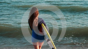 Slow motion: slim girl professional surfer comes to the sea along the beach. In the hands of yellow surfboards, dressed