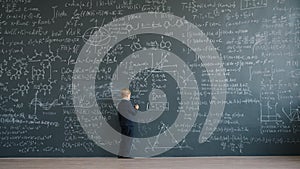 Slow motion of smart little boy writing equations on big blackboard at school