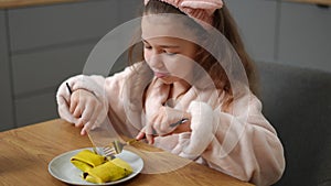 Slow motion. A smiling girl cuts a pancake with filling with a dessert knife, sitting indoors in a bathrobe and a hair