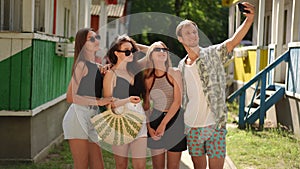 Slow motion. A smiling young man takes a selfie on his mobile phone with three girls in sunglasses, while standing