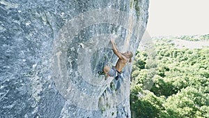 Slow motion strong muscular man rock climber dynamically climbing on a vertical cliff, making hard wide move and