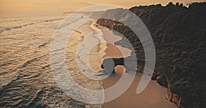 Slow motion sunset ocean seascape: waves at rock wall on sand beach aerial. Nobody nature scenery