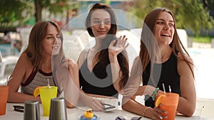 Slow motion. Three cute young women flirt while sitting at a bar counter on a summer day outdoors. The girls smiles