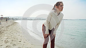 Slow motion of tired young woman taking a break while running on the sandy sea beach