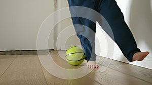 Slow motion of a toddler boy's feet running and playing with a ball on a wooden floor in a long corridor at home