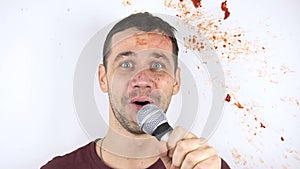 In slow motion, a tomato smashes against the face of a young stand-up comedian during his speech.