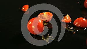 Slow motion of tomatoes falling with water drops on black surface.