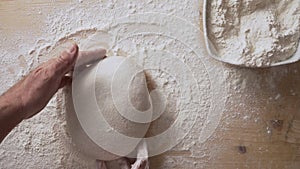 Slow motion top view of man`s hands sprinkling flour over pizza dough and massaging it to prepare it for leavening at home on a