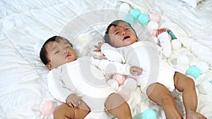 Slow-motion of two twin babies on bed, one looking, one crying