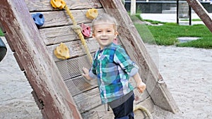 Slow motion video of cheerful smiling toddler boy playing on playground with wooden wall for climbing