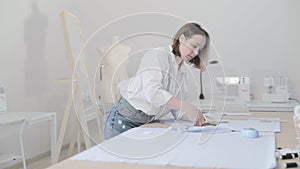 Slow motion video of the fashion designer works at a table with curves and a pattern, she are cutting fabric, around