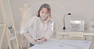 Slow motion video of the fashion designer works at a table with curves and a pattern, she are cutting fabric, around