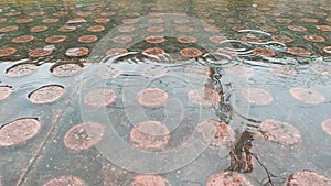 Slow-motion video of raindrops falling on a puddle created in the podotactile tiles of a station platform