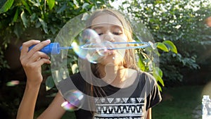 Slow motion video of smiling teenage girl blowing colorful soap bubbles in camera at sunny summer day in park