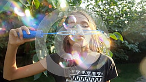 Slow motion video of smiling teenage girl in park blowing soap bubbles in camera