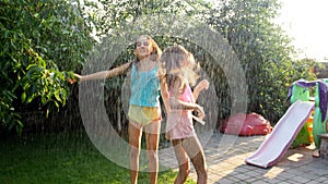 Slow motion video of two cheerful teenage girls dancing under the summer rain in sunset light