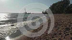 Slow motion view of beach with waves and crane boat on water
