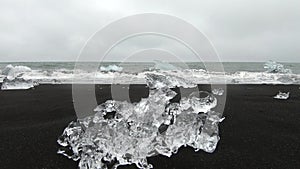 Slow motion view of melting ice crystals icebergs on black volcanic sand, Diamond beach sea waves, Jokulsarlon, Iceland