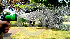 Slow motion of water coming out of a hosepipe with a garden in the background.