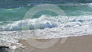 Slow motion waves breaking on sandy beach on a bright sunny day in Portugal.