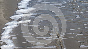 Slow motion of white foam of an ocean waves as it ends on the sand of the beach, and begins retreating back where it came from