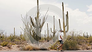 Slow motion wide shot, young tourist man walking along amazing big Saguaro cactus desert on Arizona national park road.