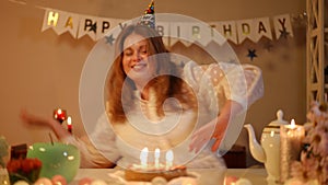 Slow motion. A woman with a birthday-cap on her head dances while sitting at a festive table. Candles are