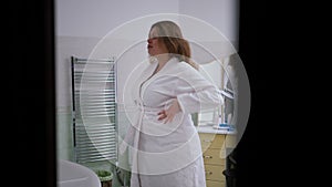 Slow motion. A woman enters the bathroom in a white bathrobe in a great mood. A woman is spinning with her arms raised