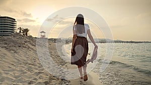 Slow motion of woman walking on the sandy sea beach at a windy day, holding a silk scarf. Beauty and peacefulness.