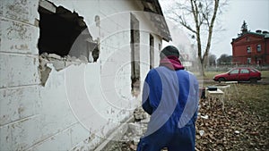 Slow motion. A worker with a hammer ruining an outside wall. Another man with a perforator working in the background