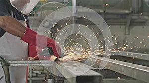 Slow motion of a worker using metal grinder with sparks flying at a metal shop