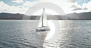 Slow motion yacht racing at ocean bay with highlang island coast aerial. Sun reflect at sailboat