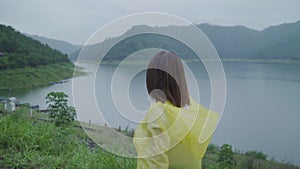 Slow motion - Young Asian woman feeling happy playing rain while wearing raincoat standing near lake.