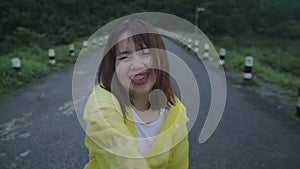 Slow motion - young asian woman feeling happy playing rain while wearing raincoat walking near forest.