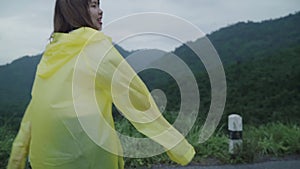 Slow motion - Young Asian woman feeling happy playing rain while wearing raincoat walking near forest.