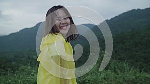 Slow motion - Young Asian woman feeling happy playing rain while wearing raincoat walking near forest.