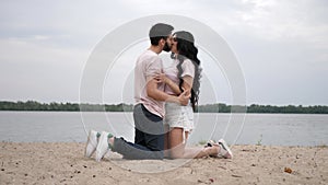 Slow motion, a young couple is kneeling on the banks of the river, hugging and enjoying each other. Happy couple in