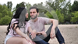 Slow motion, a young couple sits on the banks of the river, embracing and enjoying each other. Happy couple in stylish