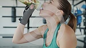 Slow motion of young female boxer drinking water during break in modern sports gym