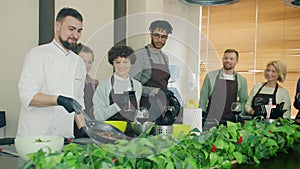 Slow motion of young man chef frying food cooking meal teaching group of trainees