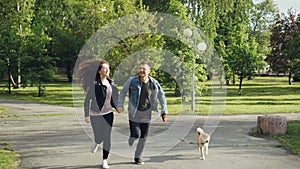 Slow motion of young married couple running in the park with small dog enjoying freedom and activity with beautiful