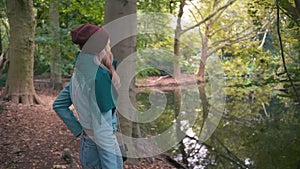 Slow Motion A young unrecognized woman girl in a red hat and blue jacket, in the fall in a park near the lake, stands