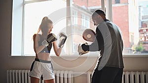 Slow motion of young woman doing boxing workout at the gym and punching her instructor, who is dodging her blows and