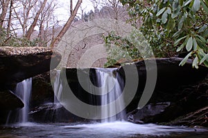 Slow Shutter Speed Photography of a Small River Waterfall with Moss Covered Rocks in the Woods.