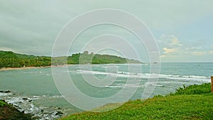 slowly panorama of blue ocean with rocky beach surrounded by green hills cloudy sky