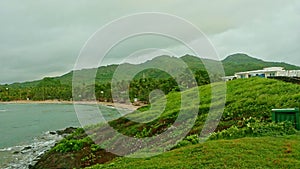 slowly panorama of blue ocean surrounded by green hills with houses and cloudy sky